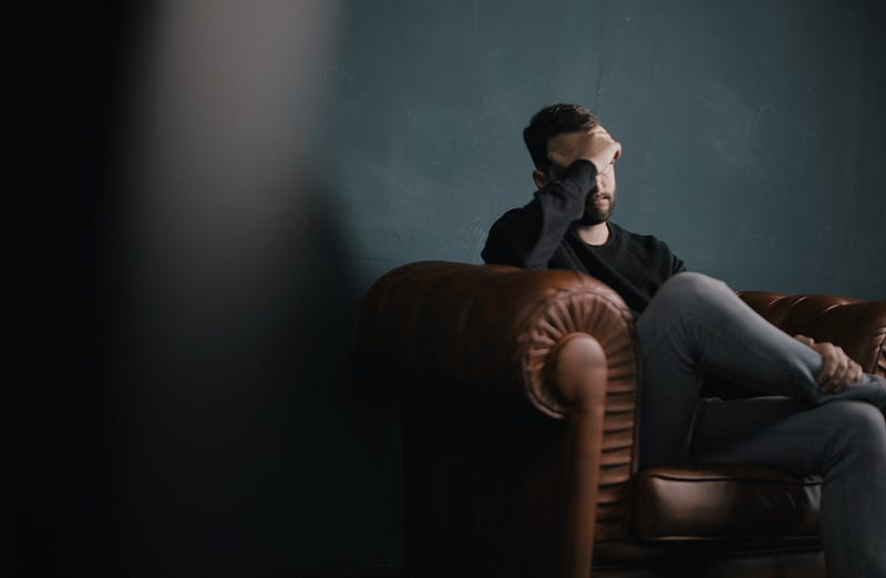 Person sitting in an arm chair with hand on head in a sad posture