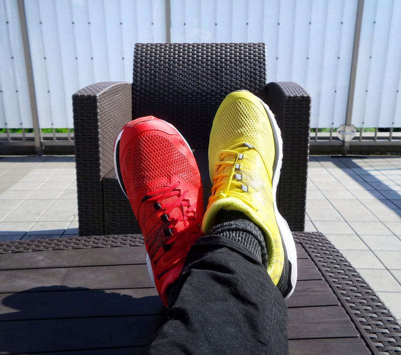 A pair of legs in different coloured trainers on each leg, yellow and red.