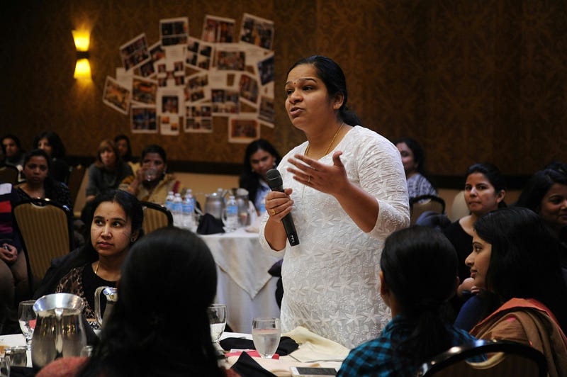A group of women sitting in diner style seats listening to a speaker holding a microphone