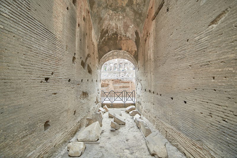 A narrow corridor showing an ancient wall of bricks on either side with a small railing on the far side.